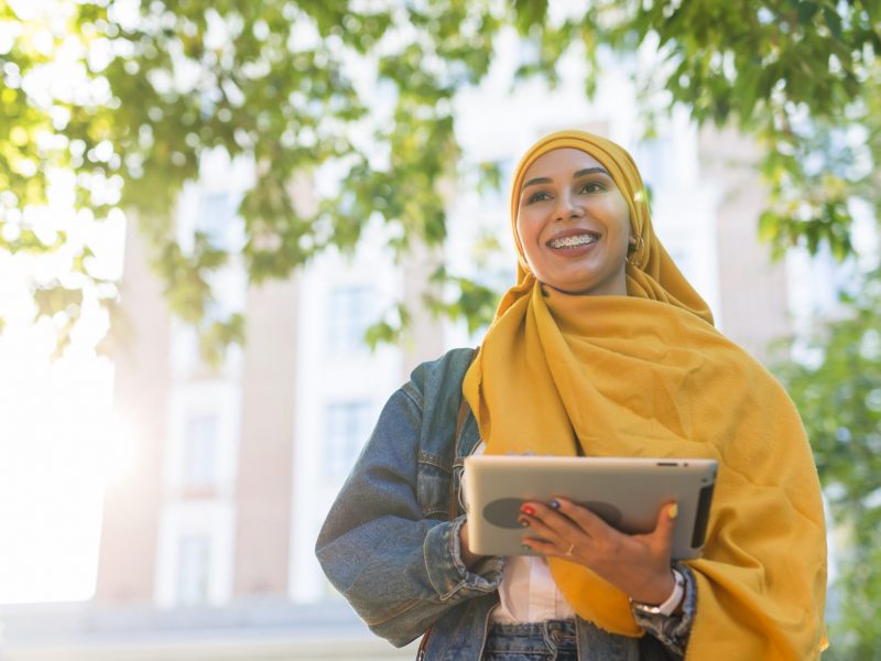 Arab woman student. Beautiful muslim female student wearing yellow hijab holding tablet